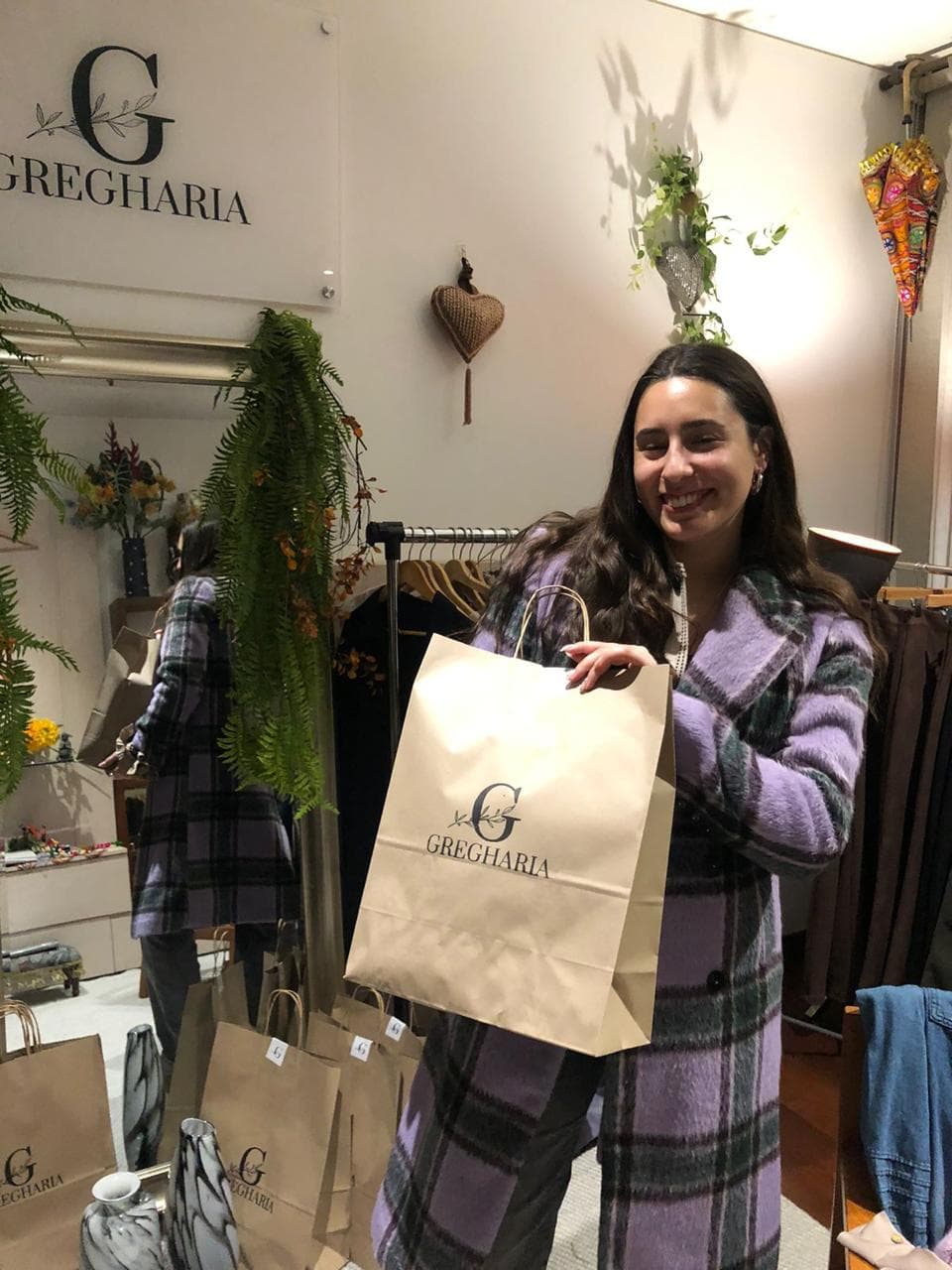 Clienta Gregharia con abrigo a cuadros morado sosteniendo una bolsa de la tienda